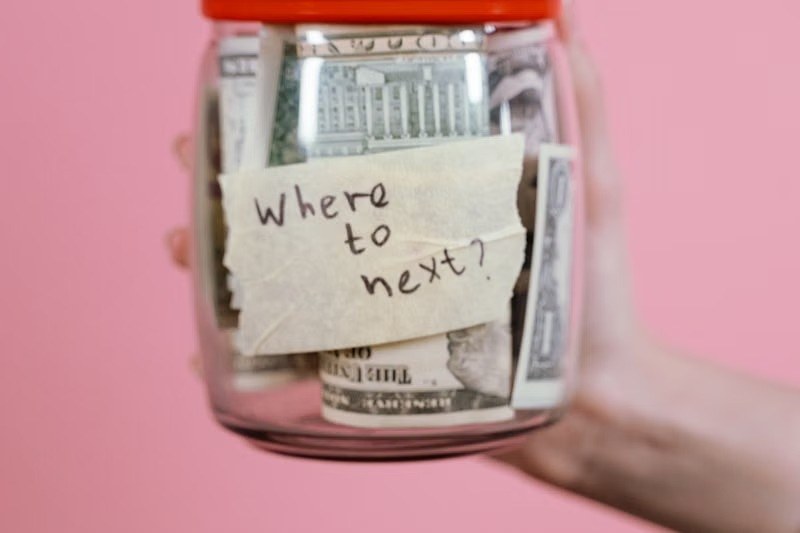 Hand holding a jar of US dollar bills labeled where to next